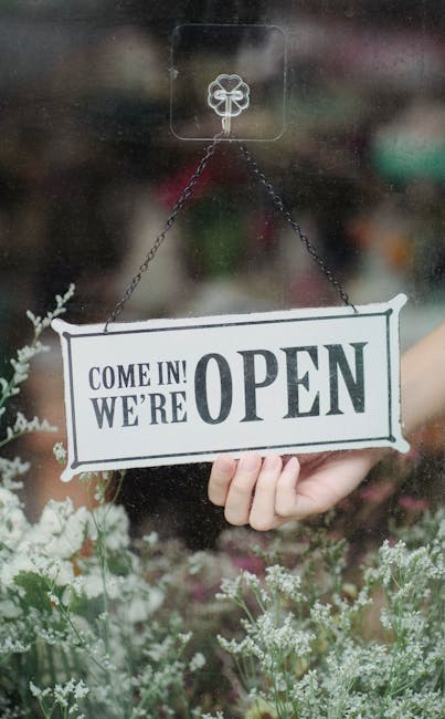 A welcoming open sign in a flower shop window with delicate blossoms in the foreground.